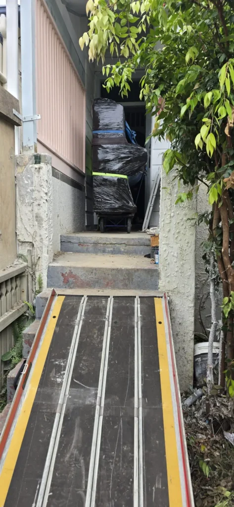Wrapped upright piano on a trolley at the top of a ramp laid over the front steps of an inner west terrace