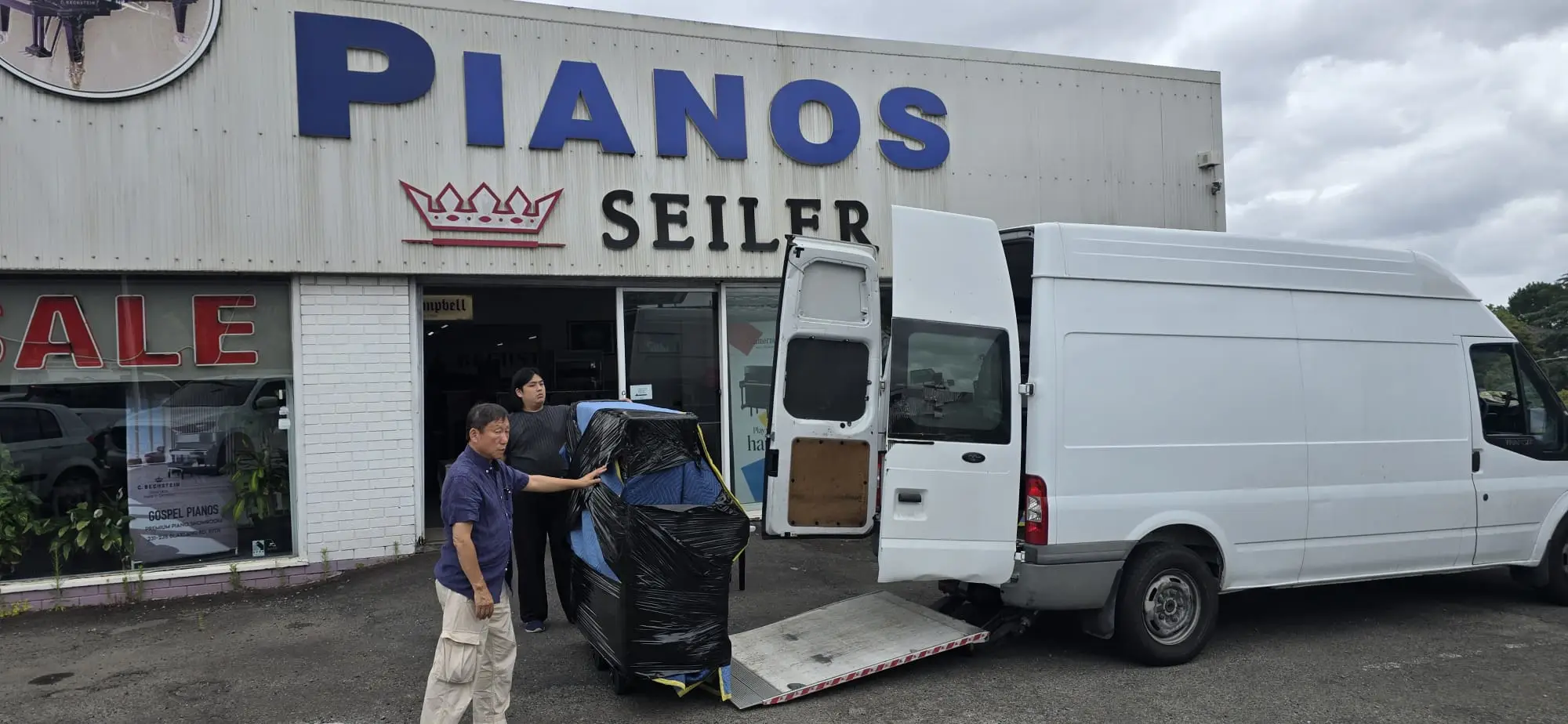 Piano being loaded onto a Piano Pickup van outside the Gospel Pianos showroom on Blaxland Road, Ryde, with Seiler and C. Bechstein signage above the entrance