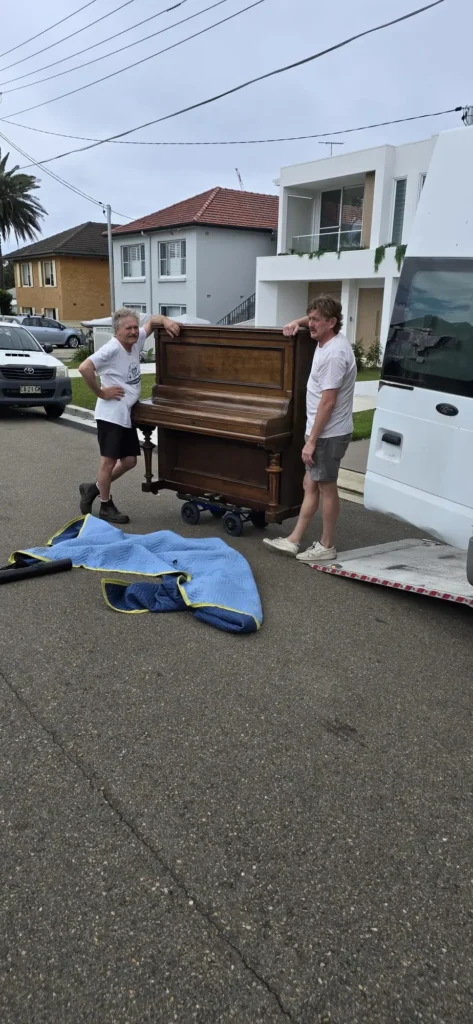 Two Piano Pickup crew loading a walnut upright piano into the truck on a Sydney street