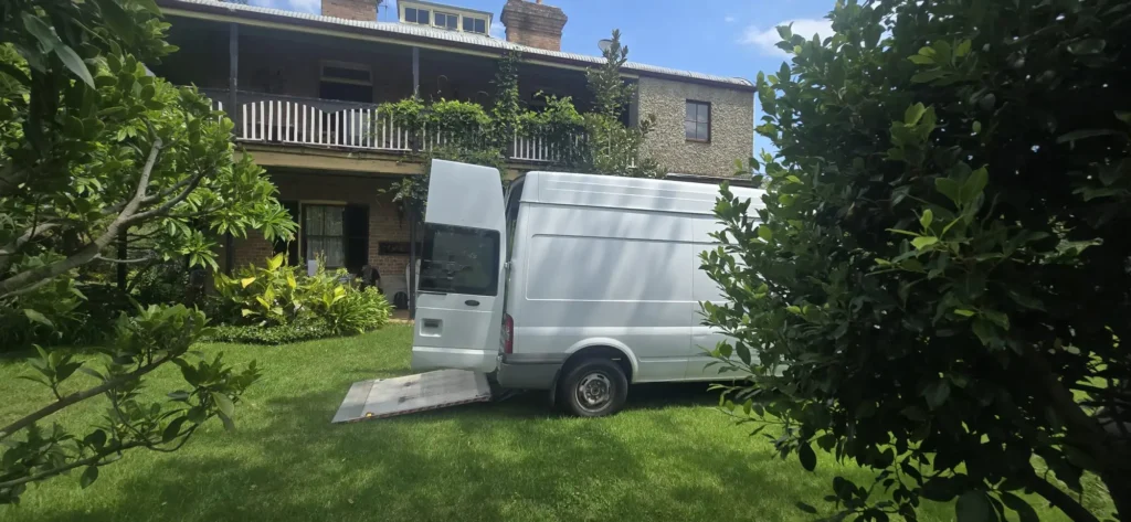 Piano Pickup van with loading ramp down on the lawn of a two-storey heritage terrace