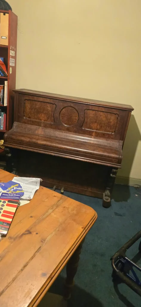 Standard size 1920s upright piano in dark burl walnut with decorative front panels, sitting against a wall in a home