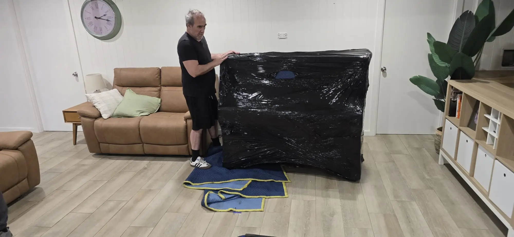 Piano Pickup mover sealing an upright piano in black protective plastic wrap over padded blankets, in a Sydney living room